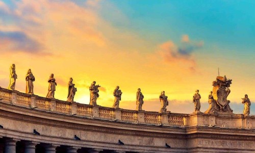 Statues on colonnades on St. Peter's Square in Vatican, Rome against colorful sunset.